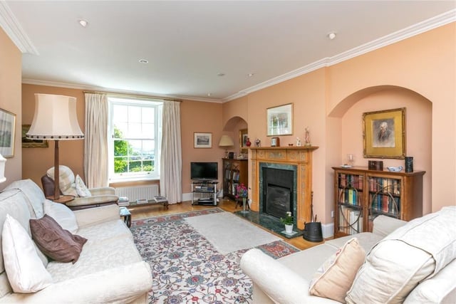 The sitting room with attractive carved fire surround, two display alcoves, shuttered windows and a wooden floor.
