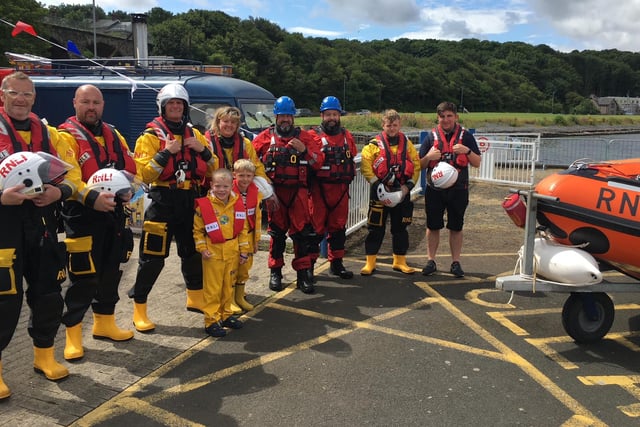 Berwick Coastguard members in their red suits with RNLI colleagues and young Miles and Toby, proudly standing with their crew member fathers.