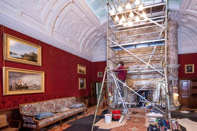 Conservator Alex Rickett climbing scaffolding to inspect the fireplace chimney breast, while Chloe Stewart carries out masonry repairs inside the inglenook.