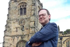 Rev Canon Paul Scott standing in front of the bell tower of St Michael's Church.