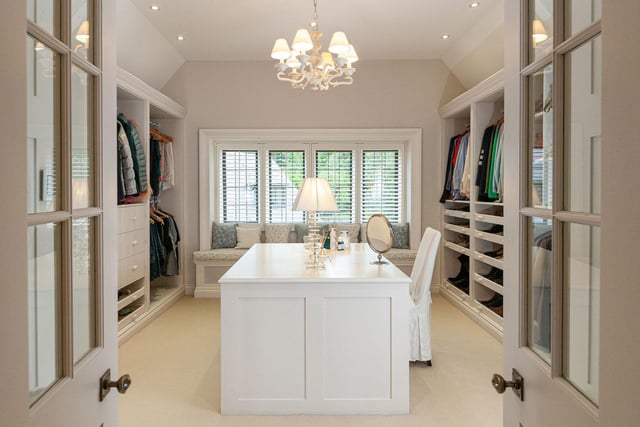 Double doors lead from the principal bedroom lead to the adjacent dressing room with an abundance of fitted storage, hanging rails, shelving, and central island with drawer storage.