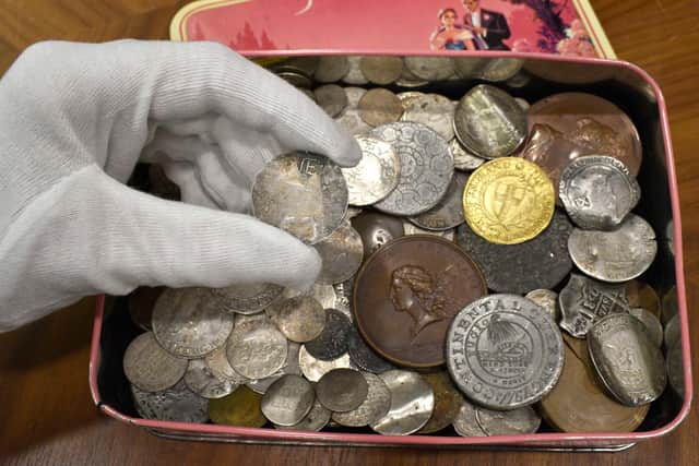The vintage sweet tin filled with coins, including the rare early American coins. The rare New England Shilling is being held.
