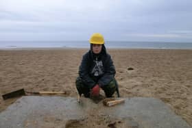 An archaeologist recording a concrete structure on the beach.