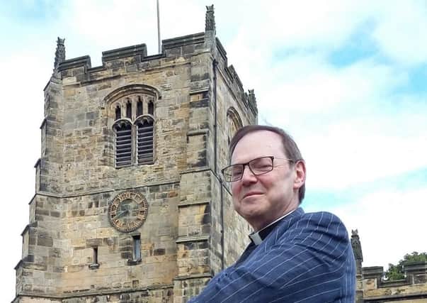 Rev Canon Paul Scott standing in front of the bell tower of St Michael's Church in the background.