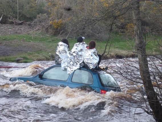 The three people wrapped in silver blankets and perched precariously on the roof of the car as the stream rages around them.