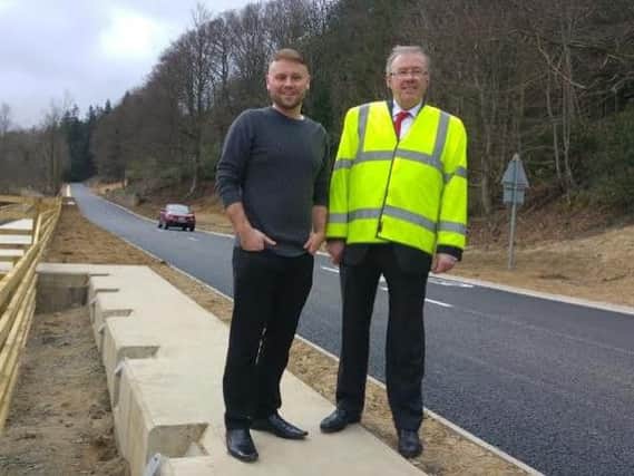 Rothbury County councillor Steven Bridgett and Coun Ian Swithenbank, Cabinet Member for Local Services, at the reopened road, with a car driving past in the background. Picture by Jane Coltman